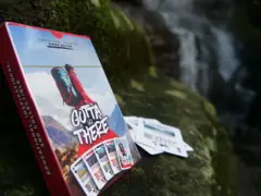 Hiking Edition box on a mossy rock by a waterfall with cards spread beside it