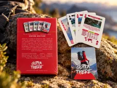 Back of the Hiking Edition box with a Joker, two Aces, the 6 of Hearts and a card back on a rock at sunset