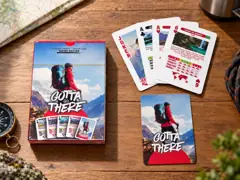 Hiking Edition box, card back, Joker, two Aces and the 6 of Hearts on a wooden table with a map and compass